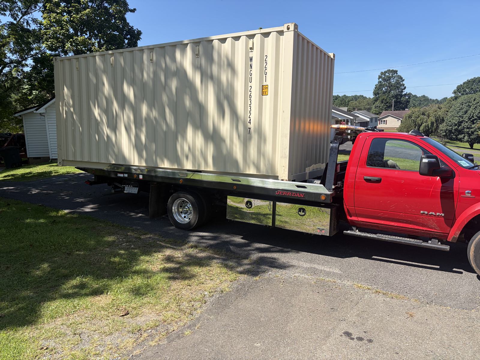 New one-trip 20-ft container arriving on a tilt-bed truck in a residential driveway